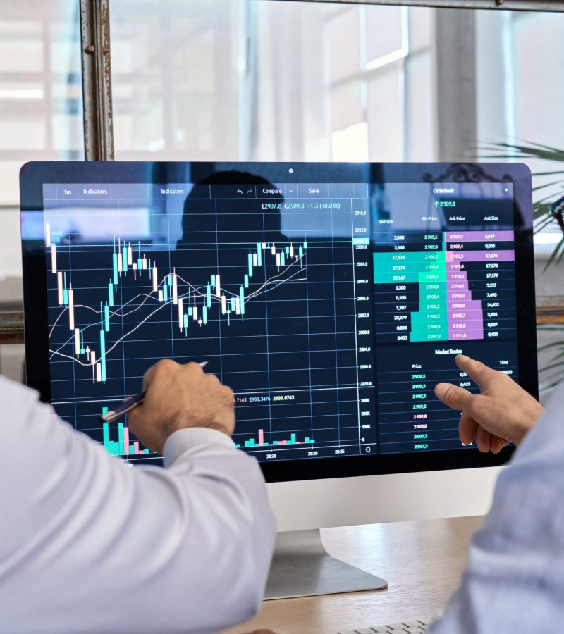 Two traders brokers stock exchange market investors discussing crypto trading charts growth using pc computer pointing at screen analyzing financial risks, investment profit forecast. Over shoulder